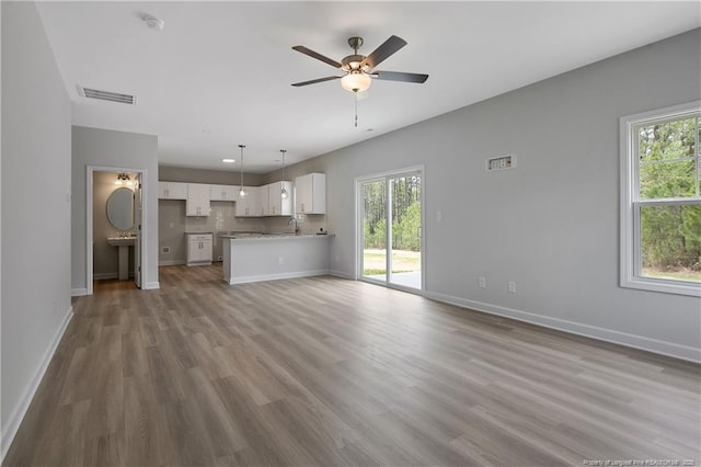 unfurnished living room featuring visible vents, wood finished floors, baseboards, ceiling fan, and a sink