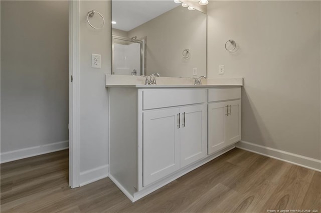 bathroom featuring double vanity, baseboards, wood finished floors, and a shower with shower door