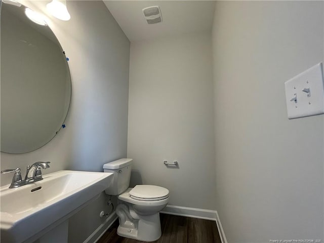 bathroom with visible vents, baseboards, toilet, wood finished floors, and a sink