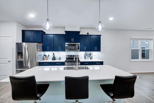 kitchen with sink, light hardwood / wood-style floors, decorative light fixtures, a kitchen island with sink, and appliances with stainless steel finishes