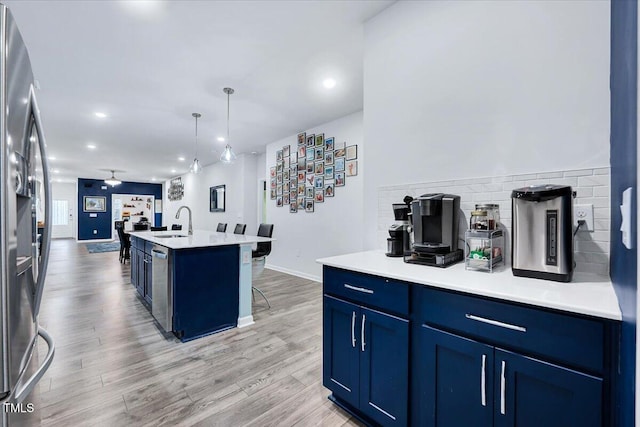 kitchen with appliances with stainless steel finishes, sink, blue cabinetry, a center island with sink, and hardwood / wood-style floors