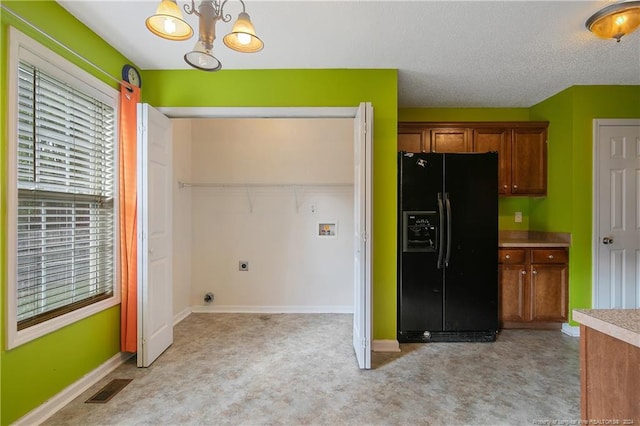 kitchen with a textured ceiling, black fridge, light carpet, and decorative light fixtures