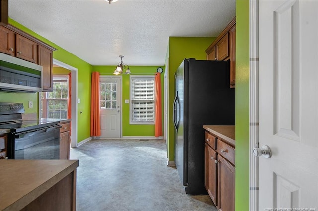 kitchen featuring pendant lighting, black appliances, a textured ceiling, and a notable chandelier