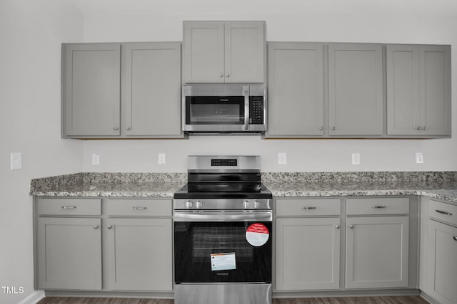 kitchen with gray cabinetry, dark hardwood / wood-style floors, light stone countertops, and stainless steel appliances