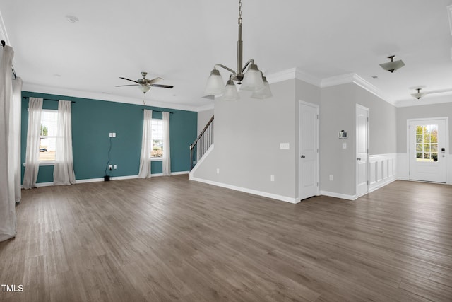 unfurnished living room featuring ceiling fan with notable chandelier, dark hardwood / wood-style flooring, ornamental molding, and a wealth of natural light