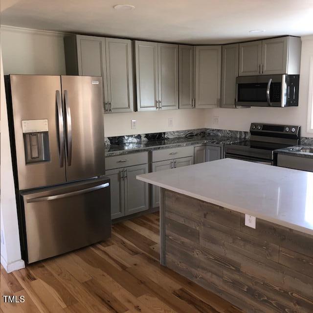 kitchen with gray cabinets, dark hardwood / wood-style flooring, dark stone countertops, and appliances with stainless steel finishes