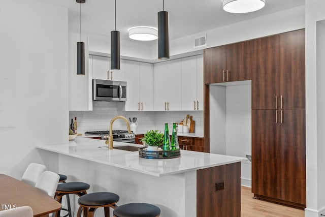 kitchen with appliances with stainless steel finishes, decorative light fixtures, dark brown cabinets, and light hardwood / wood-style floors