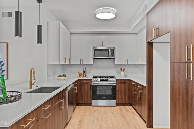 kitchen with stainless steel appliances, sink, pendant lighting, light hardwood / wood-style flooring, and white cabinetry