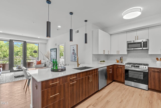 kitchen with white cabinetry, sink, decorative light fixtures, appliances with stainless steel finishes, and light wood-type flooring