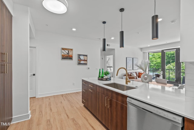 kitchen featuring stainless steel dishwasher, decorative light fixtures, light wood-type flooring, and sink