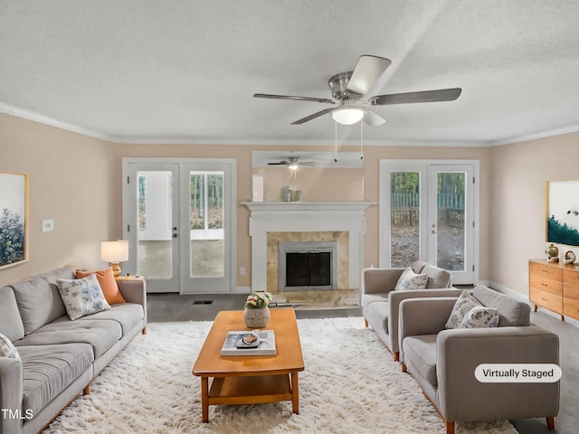 living room featuring french doors, crown molding, ceiling fan, a textured ceiling, and a tiled fireplace