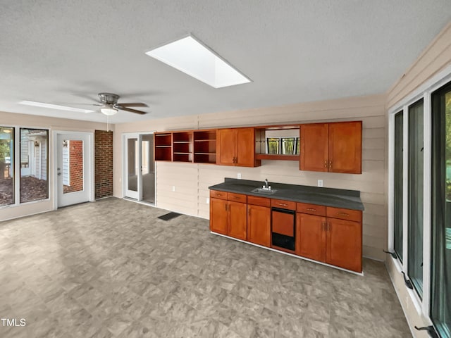 kitchen with a skylight, ceiling fan, sink, a textured ceiling, and wooden walls