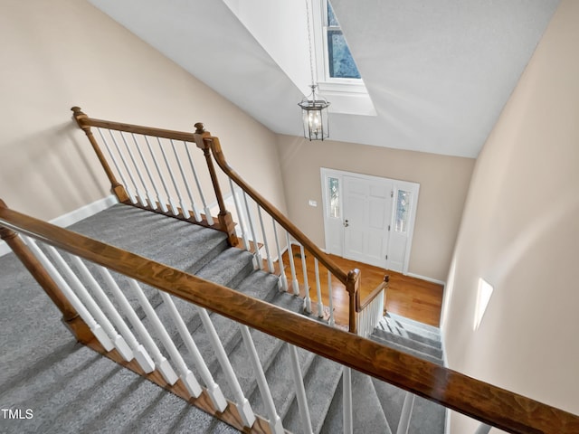 staircase featuring a chandelier, wood-type flooring, and vaulted ceiling