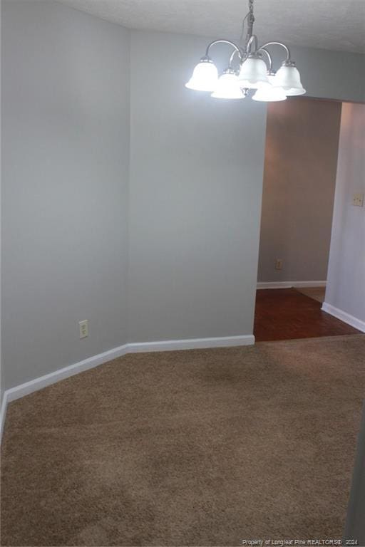 empty room featuring dark colored carpet and a chandelier