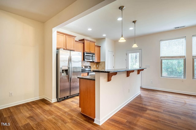 kitchen with hanging light fixtures, hardwood / wood-style floors, a kitchen bar, a kitchen island, and appliances with stainless steel finishes