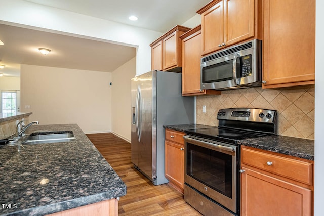 kitchen featuring decorative backsplash, light wood-type flooring, dark stone counters, stainless steel appliances, and sink