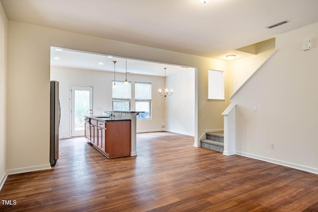 kitchen featuring sink, stainless steel appliances, hanging light fixtures, dark hardwood / wood-style flooring, and a center island with sink