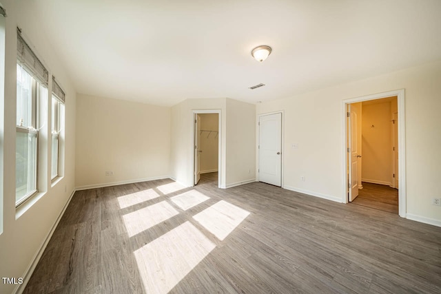 unfurnished bedroom with hardwood / wood-style flooring, a closet, a walk in closet, and multiple windows