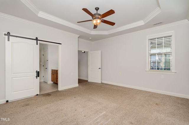 unfurnished bedroom with ensuite bath, ceiling fan, a raised ceiling, a barn door, and crown molding