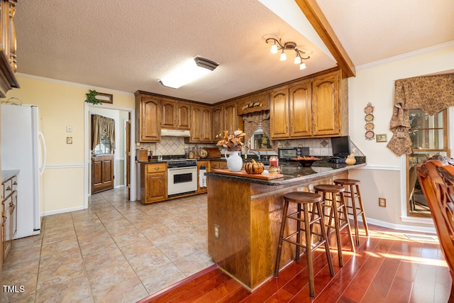 kitchen with white appliances, backsplash, crown molding, a kitchen bar, and kitchen peninsula