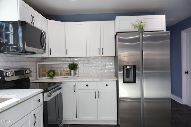 kitchen with white cabinets, dark tile patterned floors, light stone countertops, appliances with stainless steel finishes, and tasteful backsplash