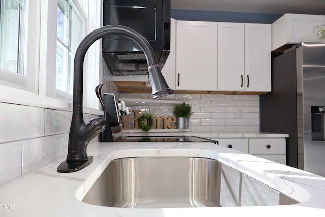 room details featuring decorative backsplash, stainless steel fridge, white cabinets, and light stone countertops