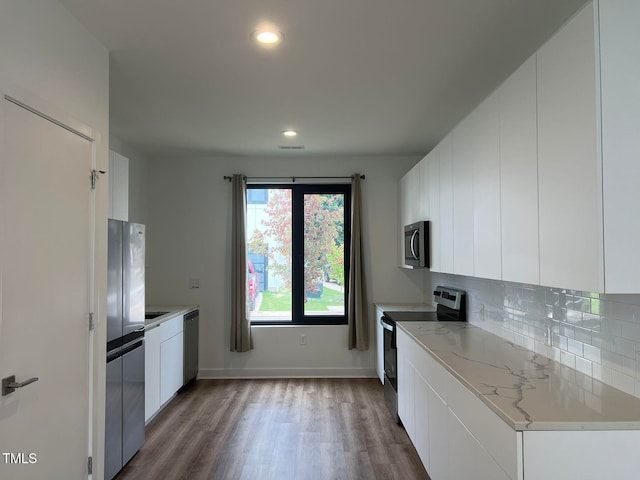 kitchen featuring light stone countertops, dark hardwood / wood-style flooring, backsplash, stainless steel appliances, and white cabinetry