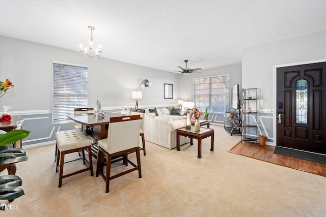 living room with a textured ceiling, light colored carpet, and ceiling fan with notable chandelier