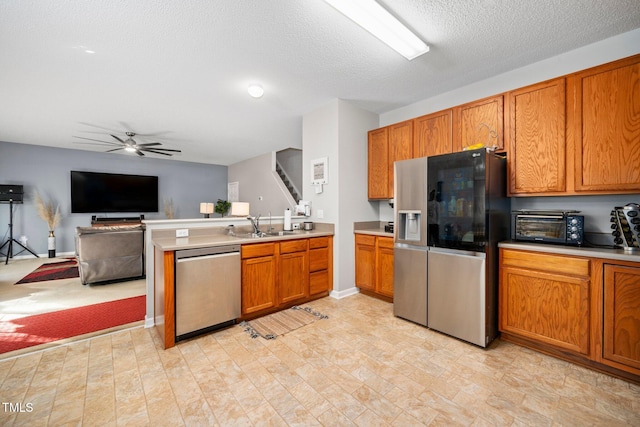 kitchen with kitchen peninsula, a textured ceiling, stainless steel appliances, ceiling fan, and sink