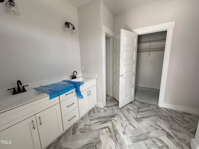 bathroom with a spacious closet, a sink, and baseboards