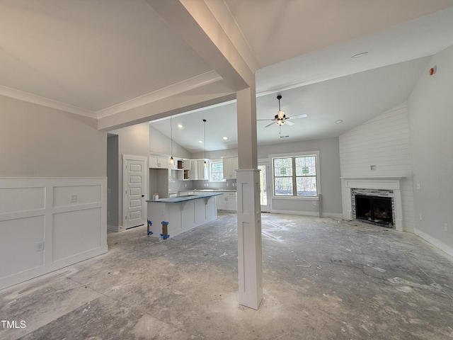 unfurnished living room featuring lofted ceiling, a fireplace, ceiling fan, wainscoting, and a decorative wall