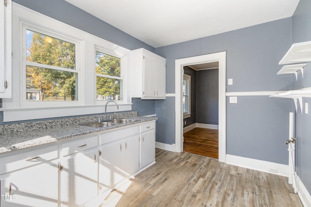 kitchen with light stone counters, light hardwood / wood-style flooring, white cabinetry, and sink