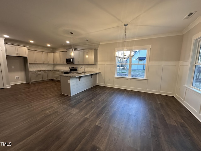 kitchen with light stone countertops, sink, stainless steel appliances, kitchen peninsula, and decorative light fixtures