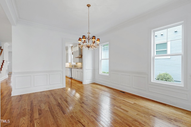 unfurnished dining area with sink, light hardwood / wood-style flooring, ornamental molding, and a chandelier