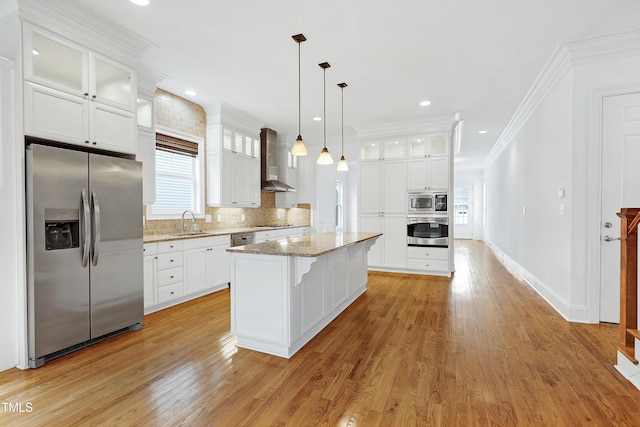 kitchen with appliances with stainless steel finishes, sink, white cabinets, a center island, and wall chimney range hood