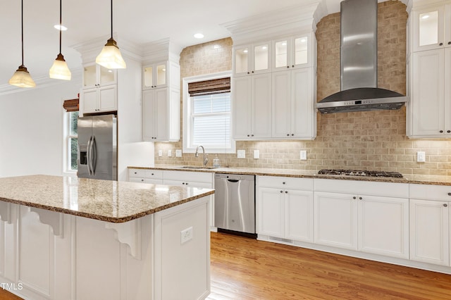 kitchen with appliances with stainless steel finishes, wall chimney exhaust hood, hanging light fixtures, and white cabinets