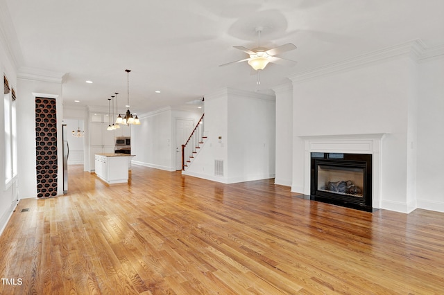 unfurnished living room featuring crown molding, ceiling fan with notable chandelier, and light wood-type flooring