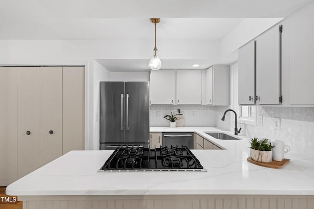 kitchen with sink, hanging light fixtures, decorative backsplash, light stone counters, and stainless steel appliances