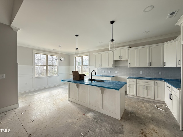 kitchen featuring a kitchen island with sink, white cabinets, ornamental molding, wainscoting, and backsplash