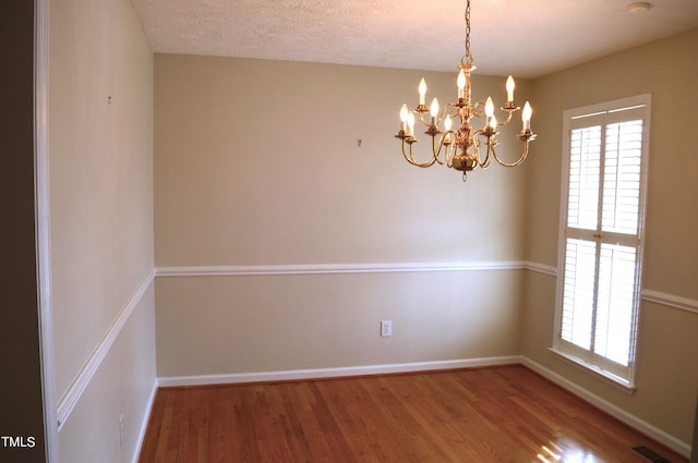 empty room featuring wood-type flooring, a textured ceiling, and an inviting chandelier