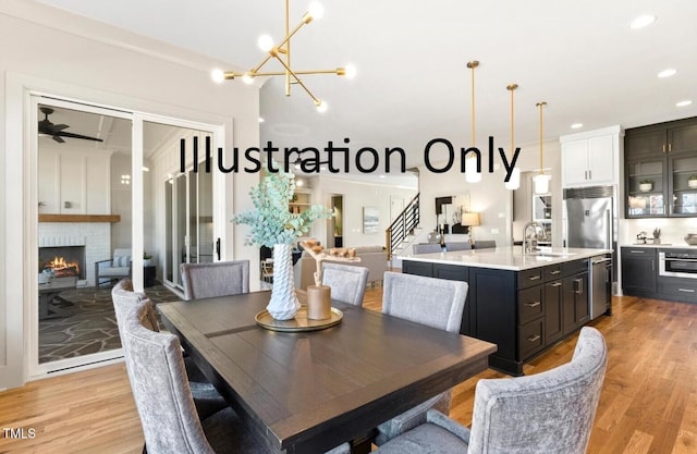 dining room with a fireplace, ceiling fan with notable chandelier, light hardwood / wood-style floors, and sink