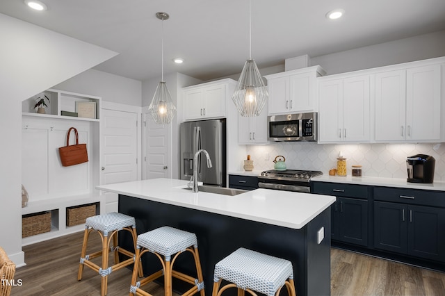 kitchen featuring white cabinetry, dark wood-type flooring, hanging light fixtures, an island with sink, and appliances with stainless steel finishes