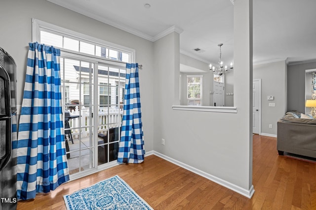 entryway featuring wood-type flooring, ornamental molding, and a chandelier