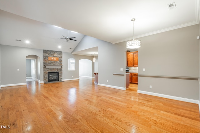 unfurnished living room with light wood-type flooring, ornamental molding, vaulted ceiling, ceiling fan, and a fireplace