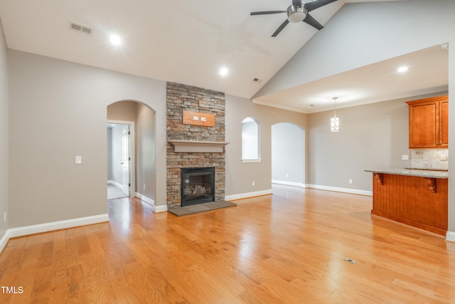 unfurnished living room featuring ceiling fan, a stone fireplace, high vaulted ceiling, light hardwood / wood-style floors, and ornamental molding