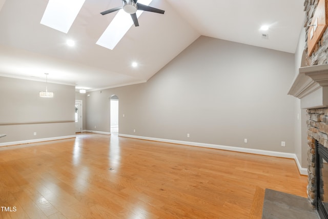 unfurnished living room with ceiling fan, light hardwood / wood-style flooring, lofted ceiling with skylight, a fireplace, and ornamental molding