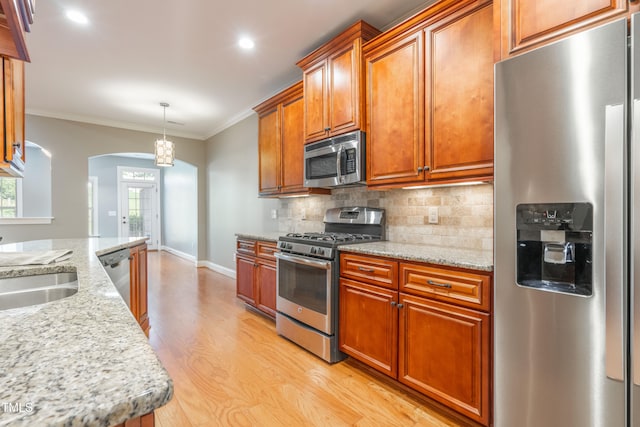 kitchen featuring light stone countertops, light wood-type flooring, ornamental molding, stainless steel appliances, and pendant lighting