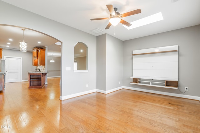 spare room featuring ceiling fan with notable chandelier, light hardwood / wood-style floors, and a skylight