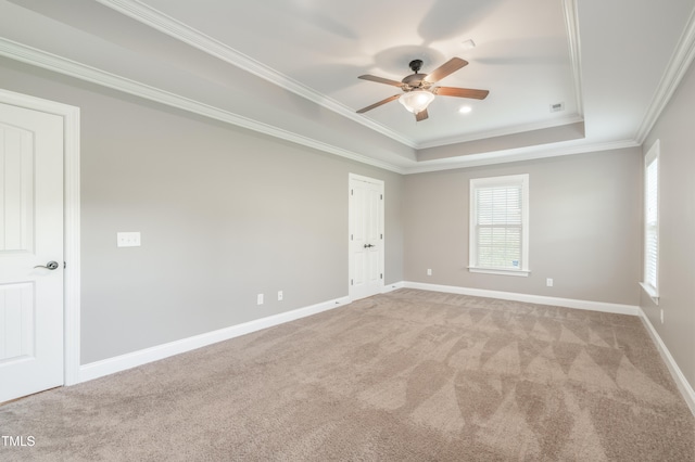 empty room with a raised ceiling, ceiling fan, light colored carpet, and ornamental molding