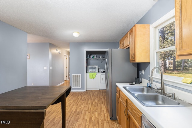 kitchen with sink, light hardwood / wood-style flooring, a textured ceiling, stainless steel appliances, and washing machine and clothes dryer